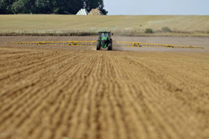 A green tractor with yellow boom arms in a field during pesticide spraying