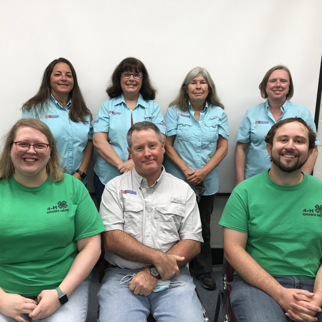 Four ladies, two with brown hair, one with grey and one blonde, all wearing light blue Extension logo shirts. Front Row is one lady in a green tshirt with blonde hair and glasses, Two men, one in a beige extension shirt, and one in a green 4-H tshirt.
