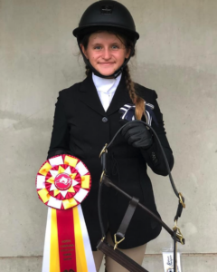 A girl in riding attire holds a ribbon.